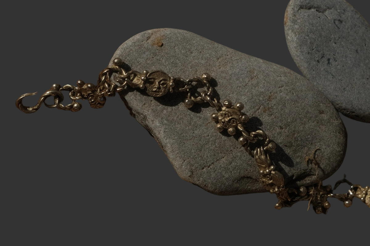 A gold chain necklace draped over two smooth gray stones on a textured brown sandy surface.